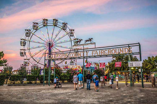 Ferris wheel and sign for Gillespie County Fairgrounds with people walking around at dusk.