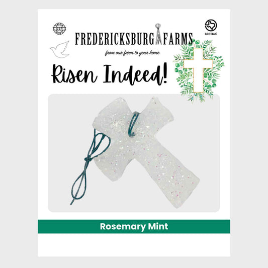 Fredericksburg Farms 'Risen Indeed!' rosemary mint scented candle packaging, featuring a clear glittery cross ornament with a dark green string on a white background.