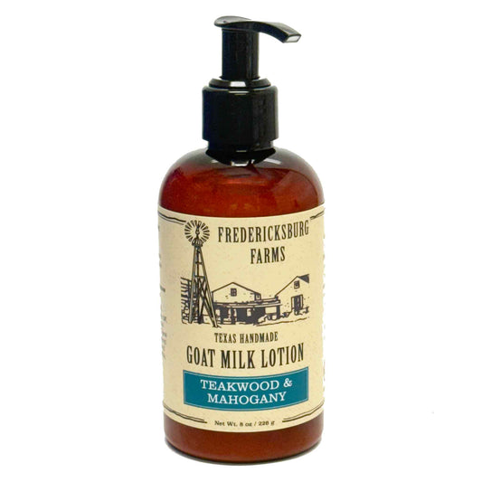 A bottle of Fredericksburg Farms Goat Milk Lotion in the Teakwood & Mahogany scent, featuring an amber glass bottle with a black pump and a cream-colored label with black text and illustrations.
